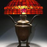 A Tiffany Studios Leaded Glass & Ember-Like Glass On Bronze Converted Oil Lamp Base. Sold For $14,100.